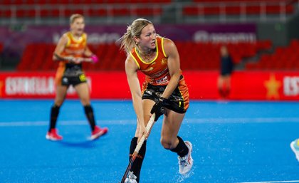 A young hockey player guiding the ball with her stick on a blue hockey field